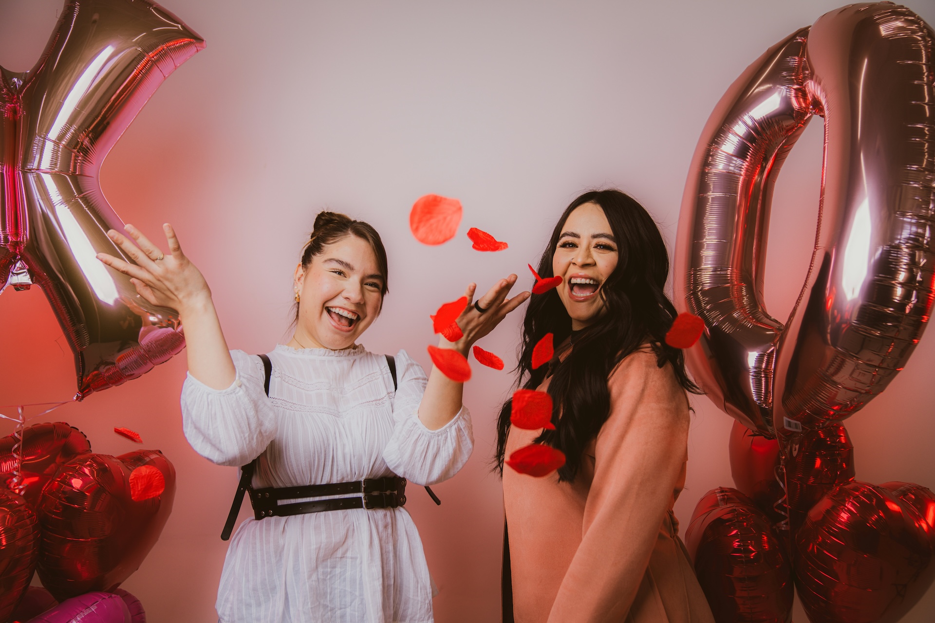 Deux femmes souriantes avec des ballons et des pétales de rose pour une fête.