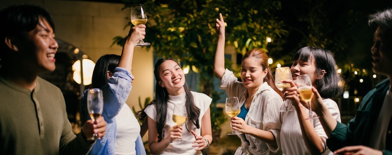 Asian friends enjoying drinks and dancing at a night party in the backyard